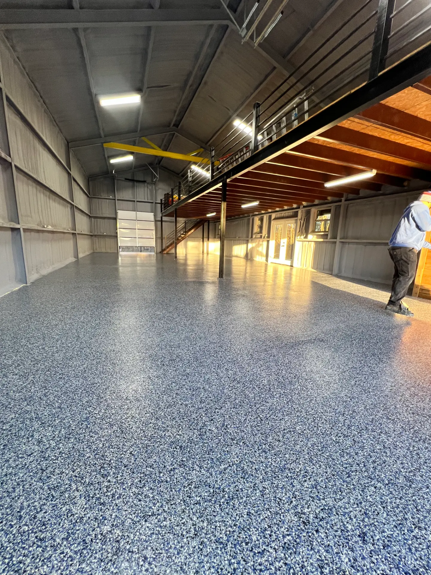 Gray and blue flake-coated floor running the length of a metal shop building with a mezzanine